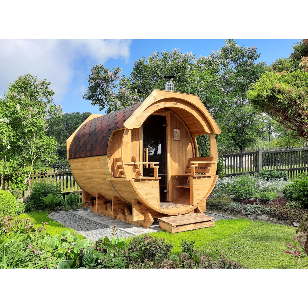 Fasssauna ALEX DE LUX im Garten, liebevoll gestaltet mit U-förmigen Sitzen und historischem Unterbau.