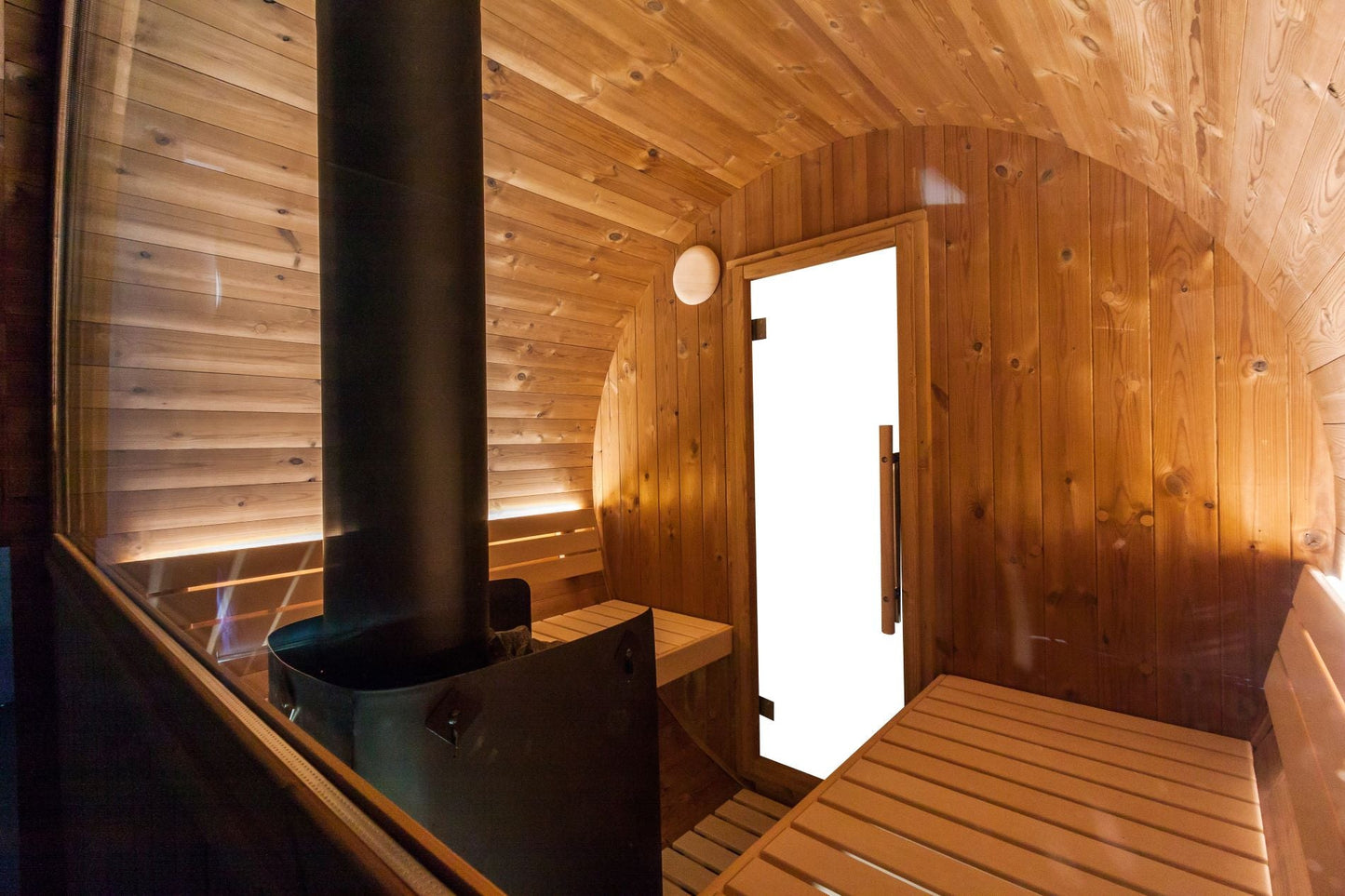 Gemütliches Innendesign der Bausatz Fasssauna KASKI 180 Halbglas-Panorama mit Holzverkleidung und Kamin.