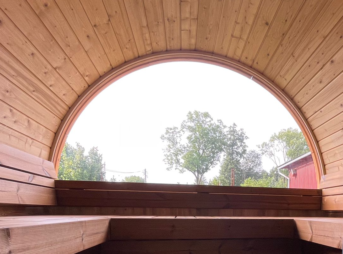 Blick aus der Fasssauna ALEX DE LUX mit großzügigem U-förmigem Sitzbereich und natürlicher Umgebung.